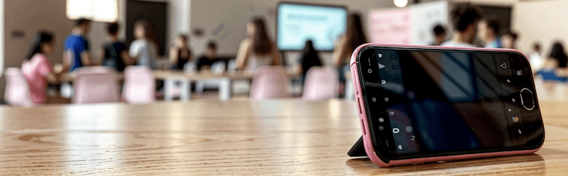 Mobile phone in landscape orientation, on a desk inside a classroom. 