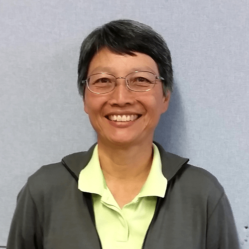 Dr Selena Chan, woman with short, dark hair and glasses stands smiling in front of a grey background